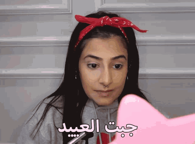 a woman wearing a red bandana and a gray hoodie with arabic writing