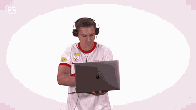 a man wearing headphones and a red bull shirt is holding an apple laptop