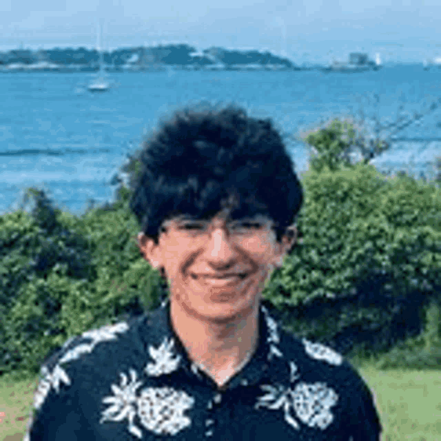 a young man wearing glasses and a black shirt is smiling in front of the ocean .