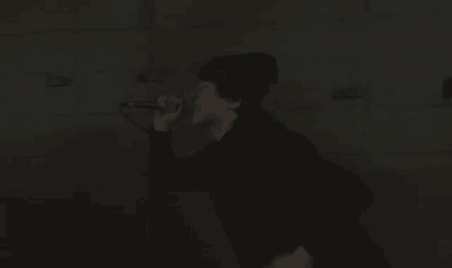 a man in a black jacket is singing into a microphone in the dark .