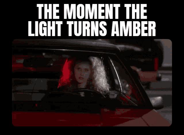 a woman is driving a red car with the words the moment the light turns amber above her