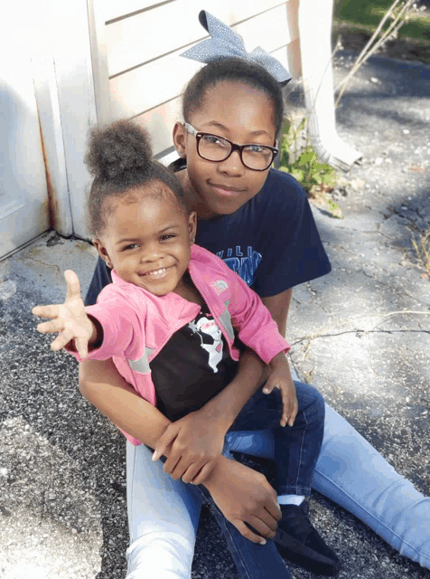 a little girl wearing glasses is holding another little girl
