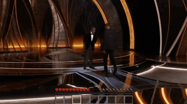 a man in a suit is standing on a stage while another man stands behind him