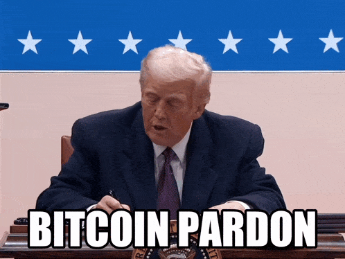 a man in a suit and tie is sitting at a desk with a sign that says bitcoin pardon in front of him