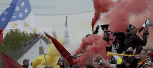 a crowd of people holding megaphones and smoke bombs with a flag in the background that says ' canadian ' on it
