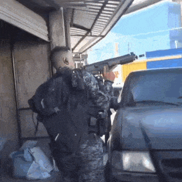 a man in a military uniform holds a gun in front of a vehicle