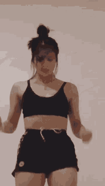 a woman in a crop top and shorts is dancing in front of a white wall .