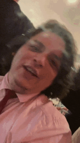 a man in a pink shirt and red tie is smiling for the camera