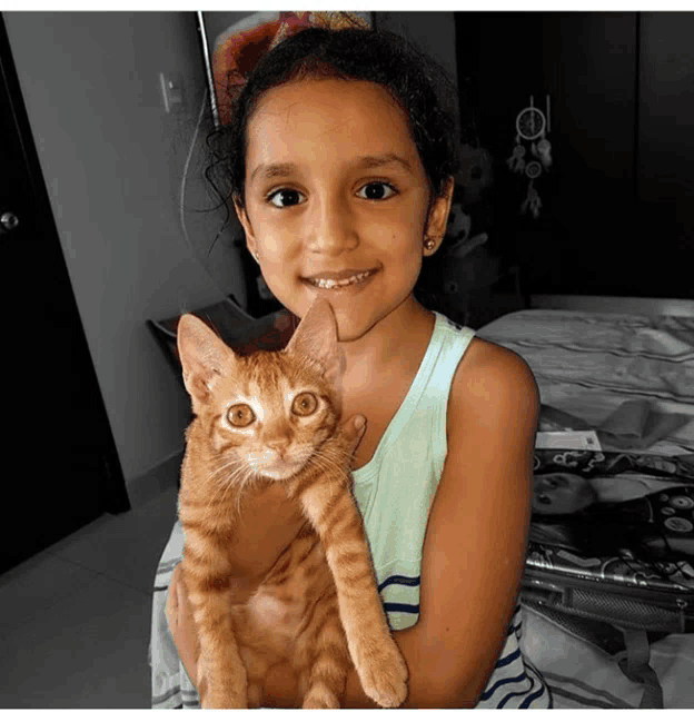a little girl is holding an orange cat in her arms and smiling