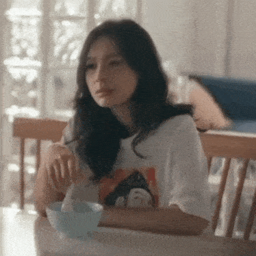 a woman in a white shirt is sitting at a table with a bowl of cereal .