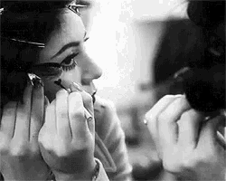a black and white photo of a woman applying makeup to her face .