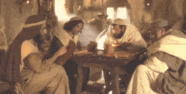 a group of men are sitting around a table talking .