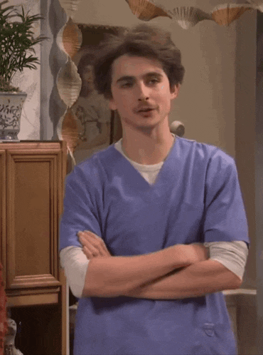 a man in a blue scrub top has his arms crossed in front of a plant