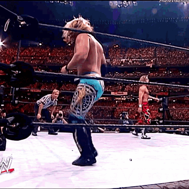 two men are wrestling in a wrestling ring with a referee in the background .
