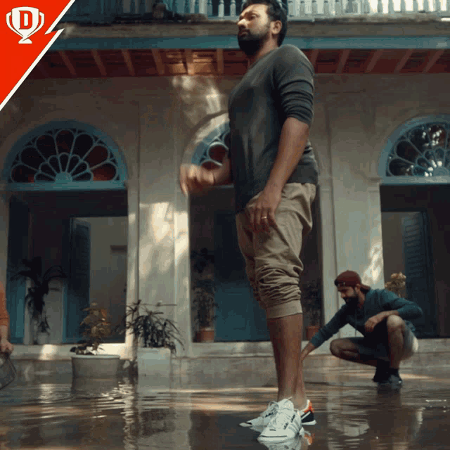 a man is standing in a puddle of water while another man squats in front of him