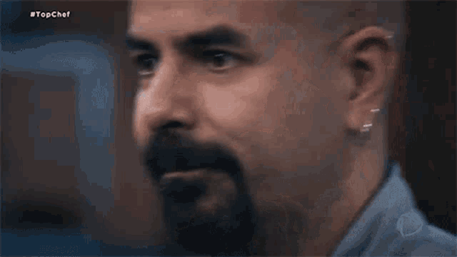 a close up of a bald man with a beard and earrings .