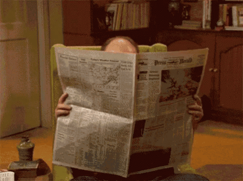 a man is sitting in a chair reading a newspaper called the press-herald