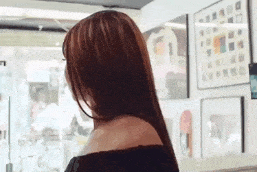 a woman with long red hair is standing in front of a window in a room with paintings on the wall .
