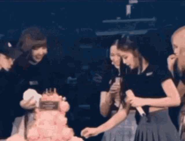 a group of people are standing around a pink cake .