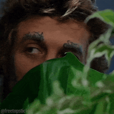 a man with a tattoo on his forehead is looking through a window .