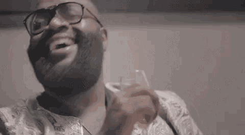 a man with a beard and glasses is holding a glass of wine in his hand .