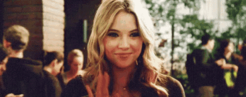 a woman is smiling and waving at the camera in front of a crowd .