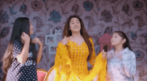 a woman in a yellow dress is dancing with two other women in a room .