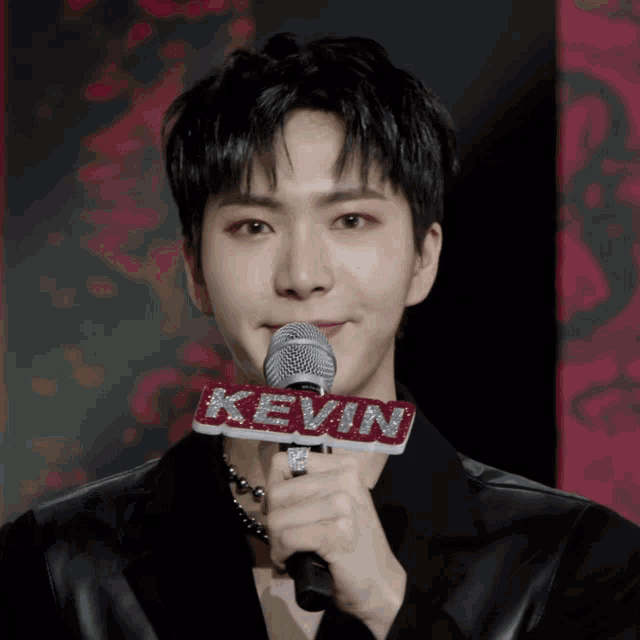 a man in a black jacket holds a microphone with the name kevin on it