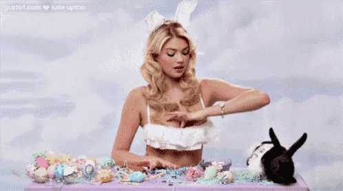 a woman in a bikini is sitting at a table with easter eggs and a bunny .