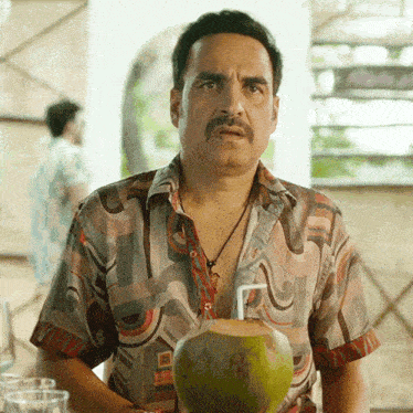 a man in a colorful shirt is holding a coconut with a straw in it