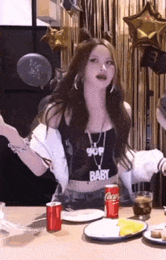 a woman is sitting at a table with plates , a can of coca cola and a glass of water .