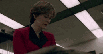 a woman in a red jacket is sitting at a table reading a book .