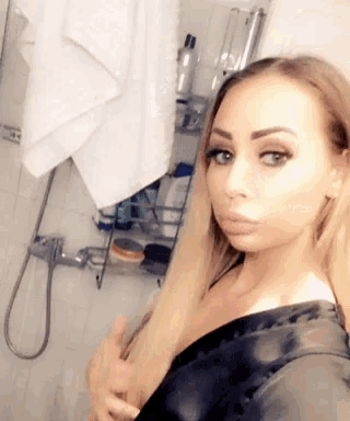 a woman taking a selfie in a bathroom with a towel hanging on the wall behind her