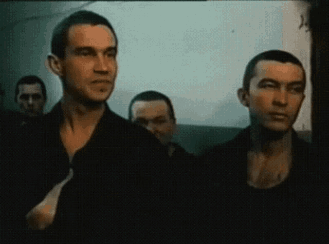 a group of men are standing in a room and one of them has a shaved head