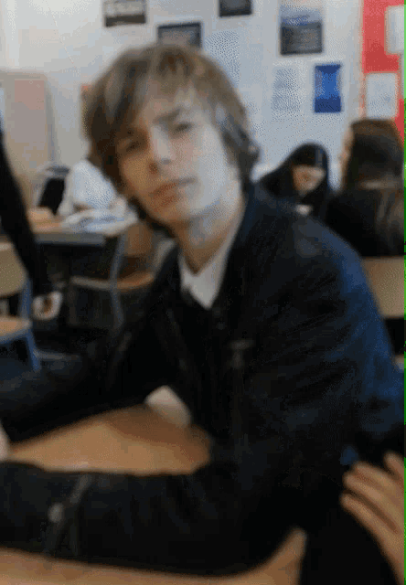 a boy in a black jacket sits at a desk