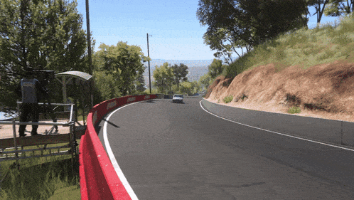 a car is driving down a curvy road with a red barrier on the side