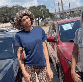 a woman wearing a leopard print hat and leopard print pants is standing in front of a red car .
