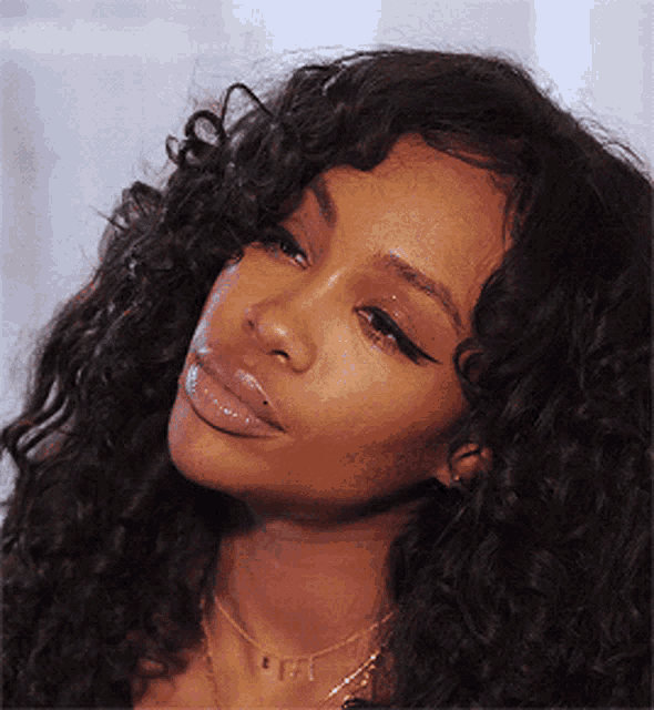 a close up of a woman 's face with curly hair and a necklace with the letter f on it