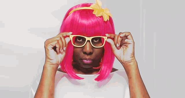 a woman wearing a pink wig and yellow glasses looks over her glasses