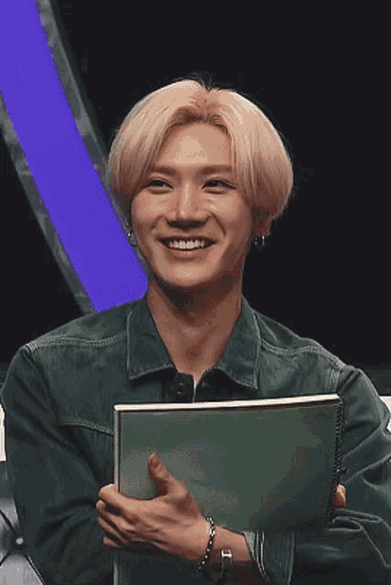 a young man with blonde hair is smiling while holding a green book