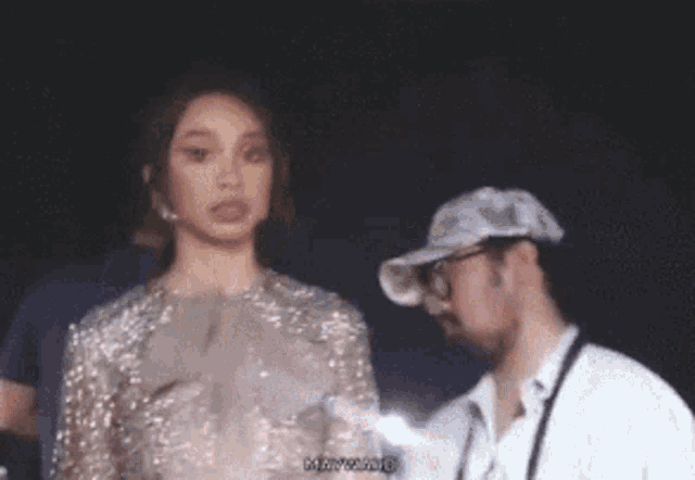 a woman in a sequined dress is standing next to a man wearing a baseball cap .