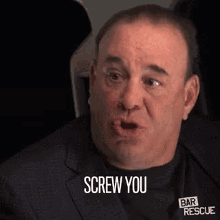 a man in a suit and black shirt is making a funny face and says `` screw you '' .