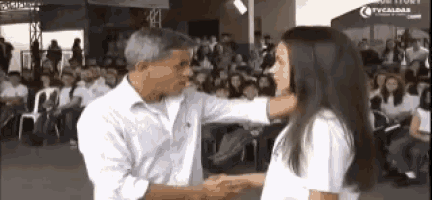 a man and a woman are shaking hands in front of a crowd with a tvcaldas sign in the background