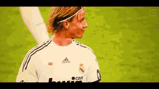 a man wearing a white adidas shirt stands on a green field