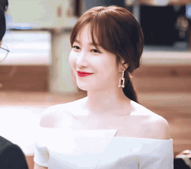 a woman is wearing a white off the shoulder top and earrings .