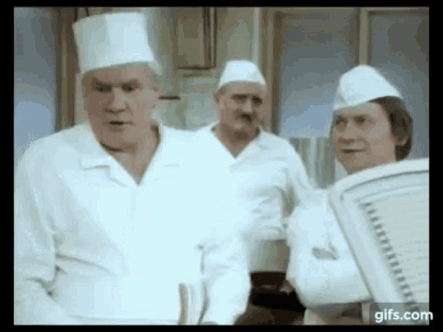 a group of three men in chef 's hats are standing in a kitchen .