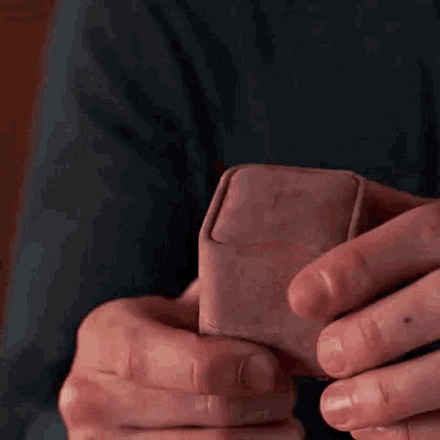 a person is holding a pink box with an engagement ring in it .