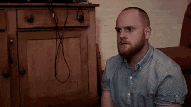 a man with a beard is sitting in front of a cabinet