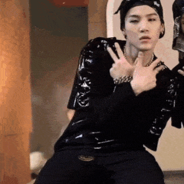 a young man in a black shirt and black pants is giving a peace sign with his hands .