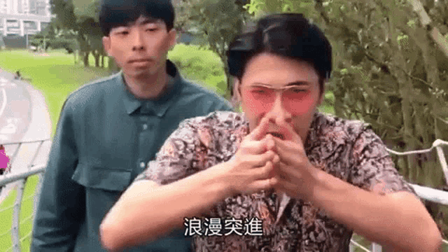 a man wearing red sunglasses is making a funny face while another man stands behind him .
